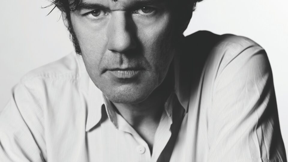 headshot of Stefan Sagmeister; black/white image of a man wearing a white collared shirt, leaning forward, looking into camera