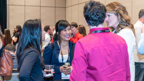Group of four smiling people facing each other and mid-conversation in a crowded room.