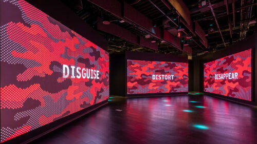 Immersive exhibition designed by Local Projects with digital camouflage visuals and the words disguise, distort, and disappear.
